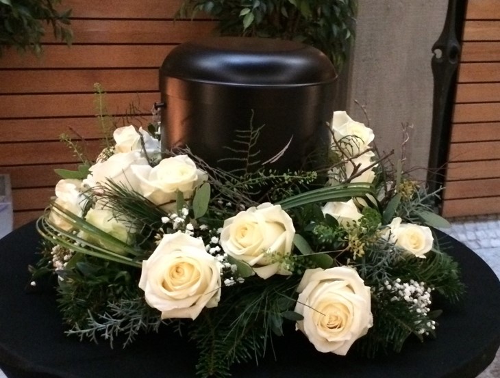 Schwarze Urne mit wei&szlig;en Rosen auf floralem Trauerarrangement
