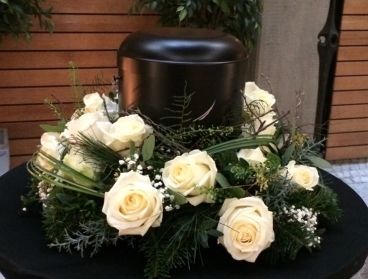 Schwarze Urne mit wei&szlig;en Rosen auf floralem Trauerarrangement